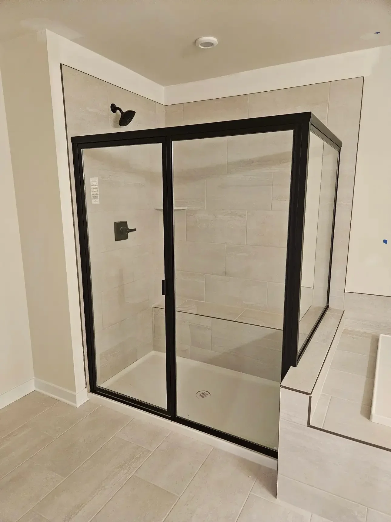 Frameless glass shower enclosure with black frame, ceramic tile surround, and rainfall showerhead