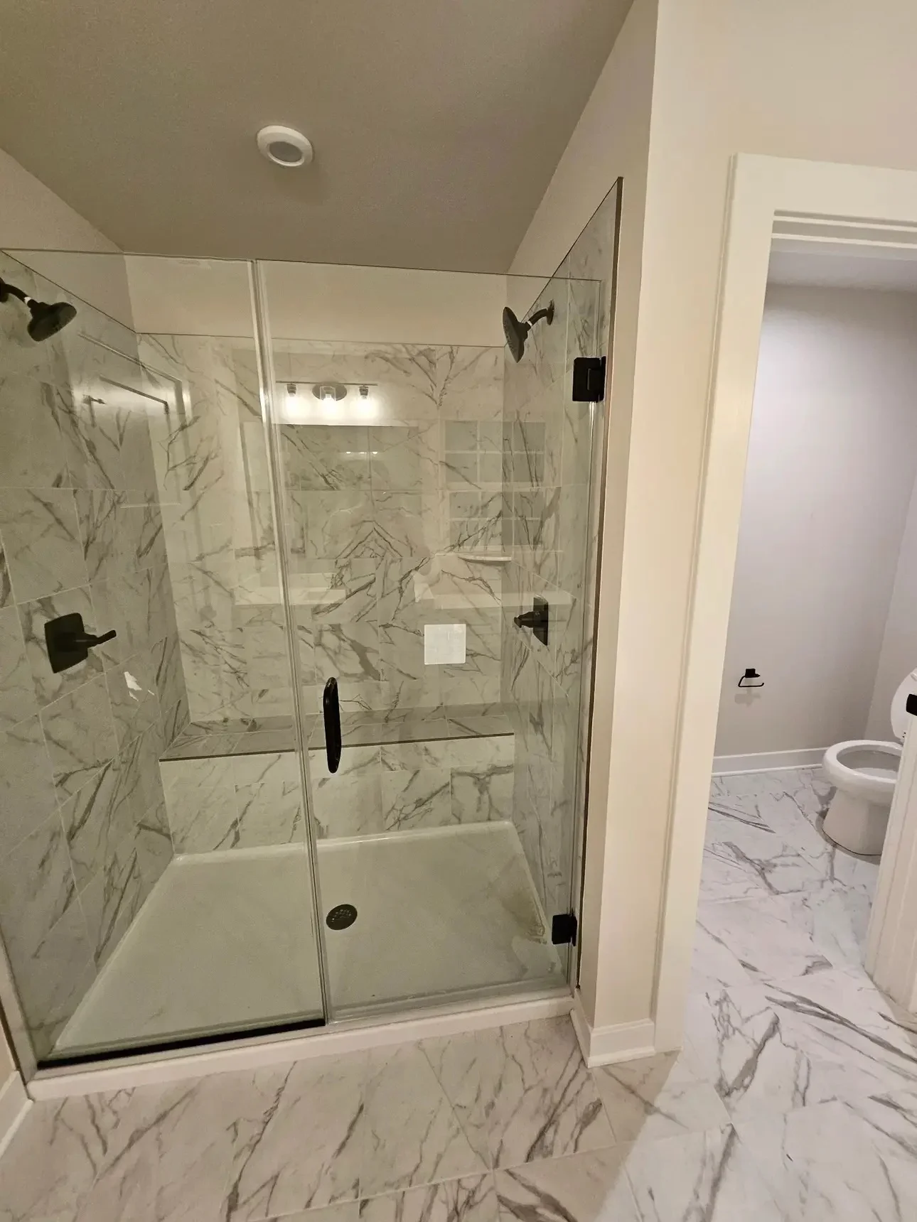 Marble tile walk-in shower with frameless glass doors and black hardware fixtures