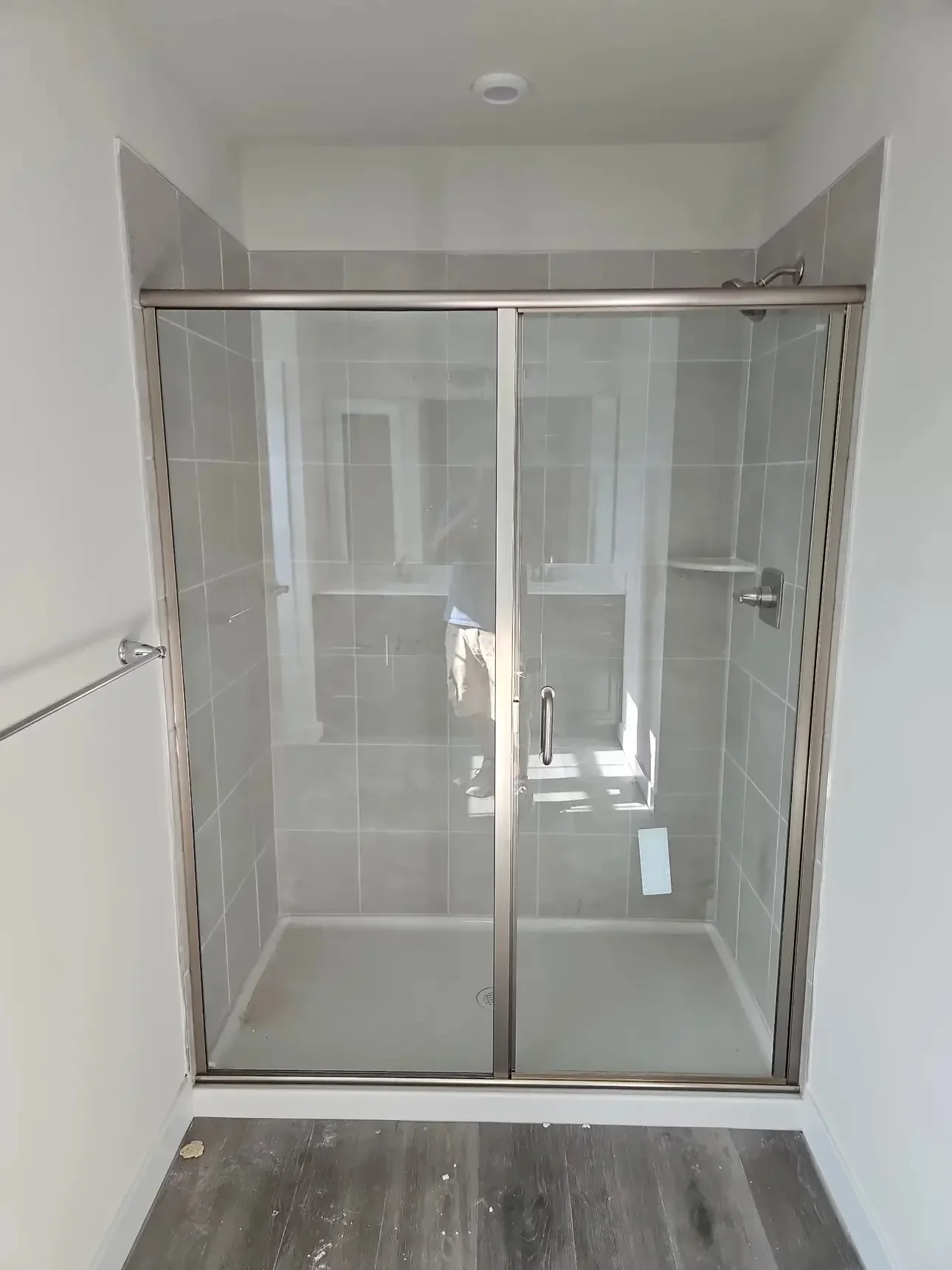 Frameless glass shower enclosure with sliding doors, gray subway tile, and brushed nickel hardware