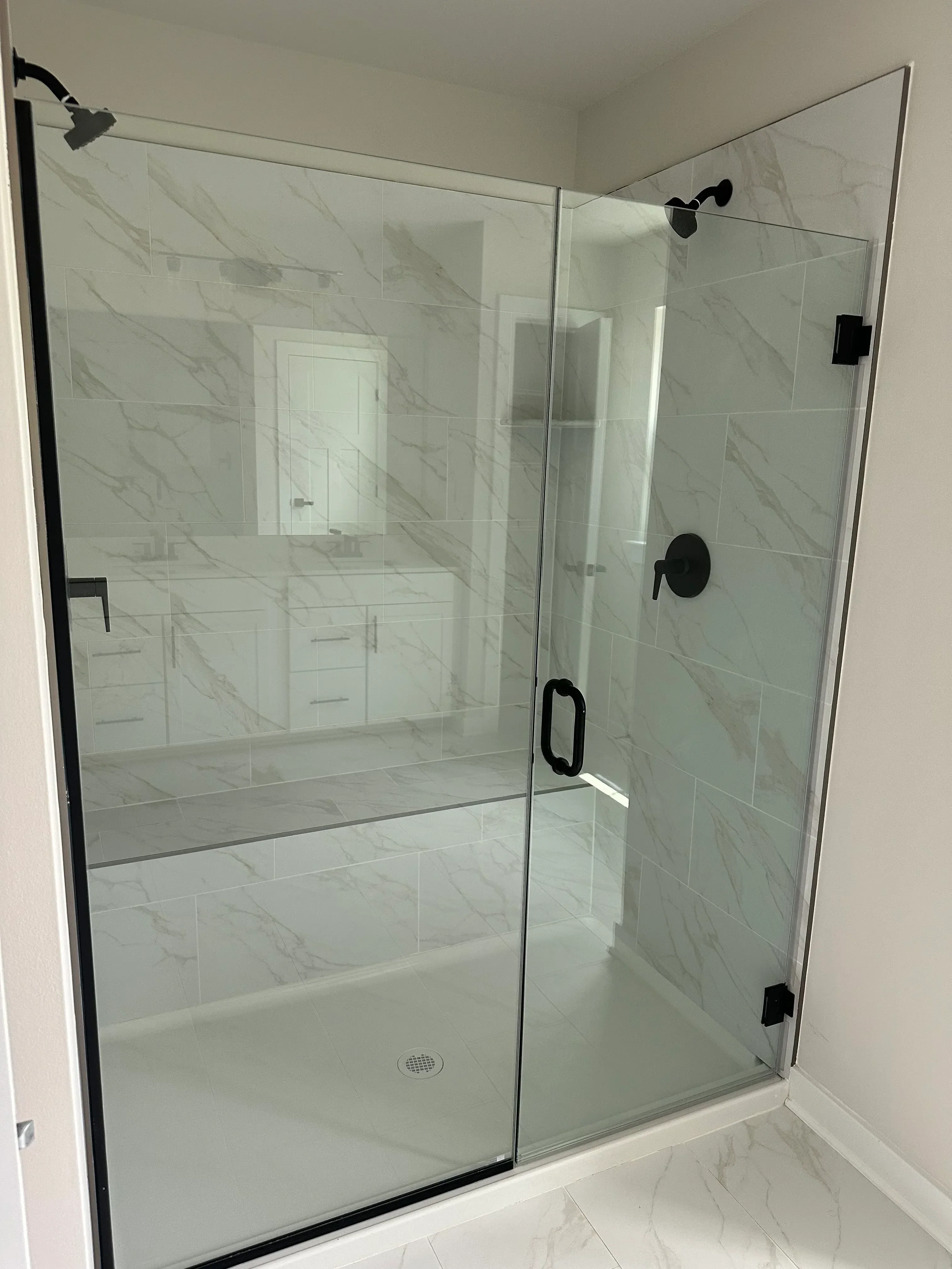 Frameless glass shower enclosure with marble tile walls and black hardware fixtures