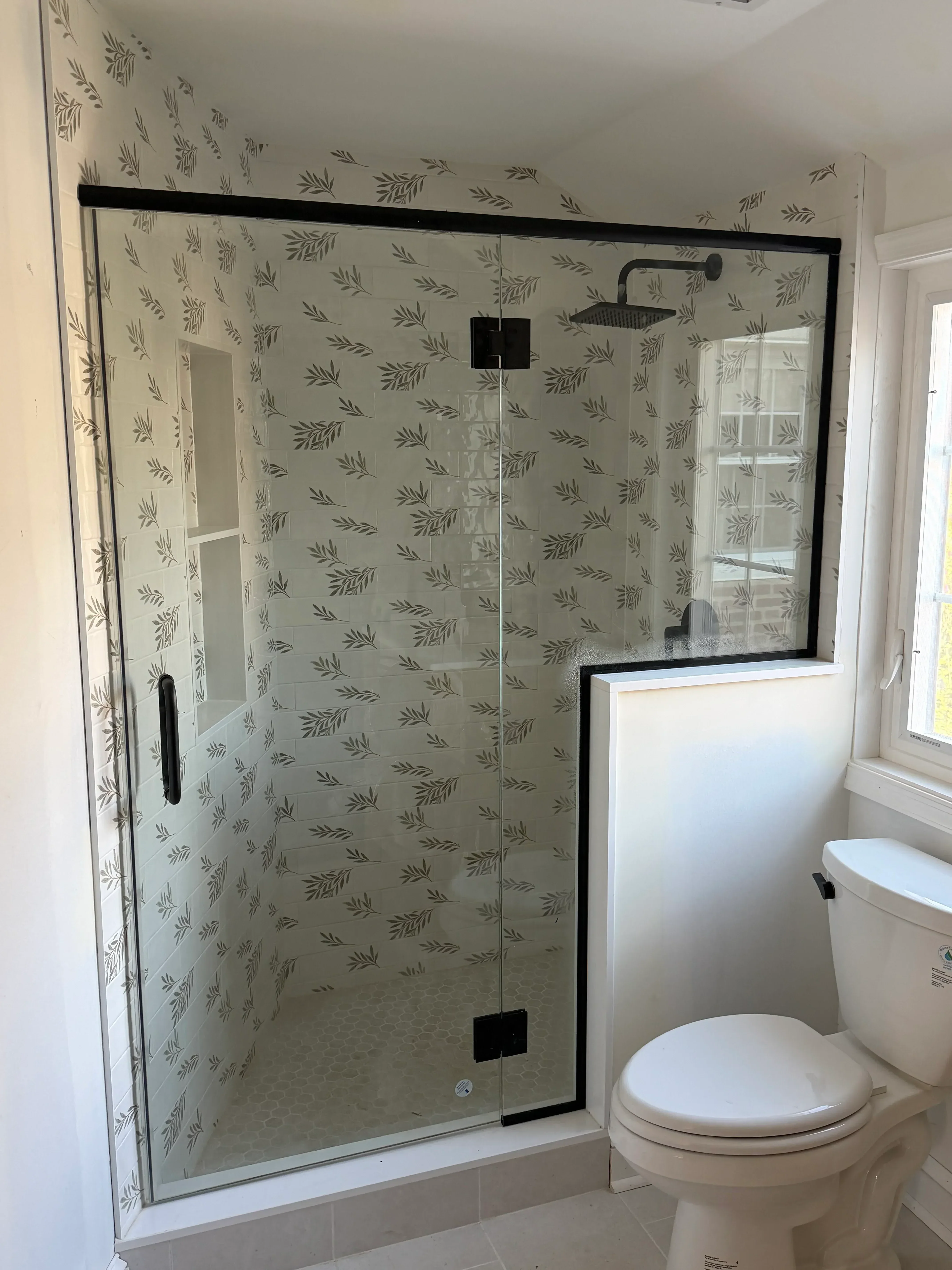 Frameless glass shower enclosure with black hardware and leaf-pattern ceramic tile walls