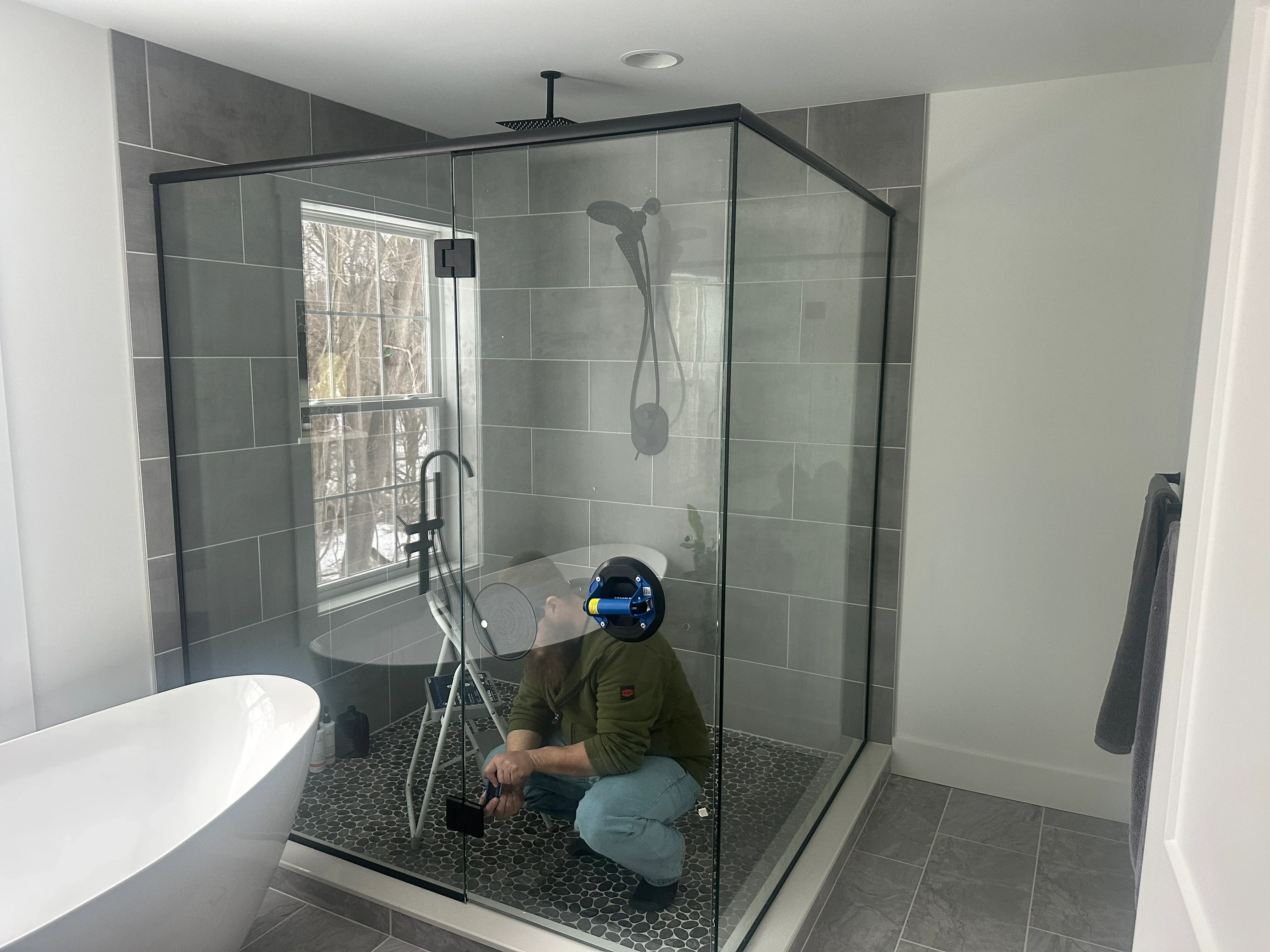 Frameless glass shower enclosure with gray subway tile walls and black hexagonal floor tile