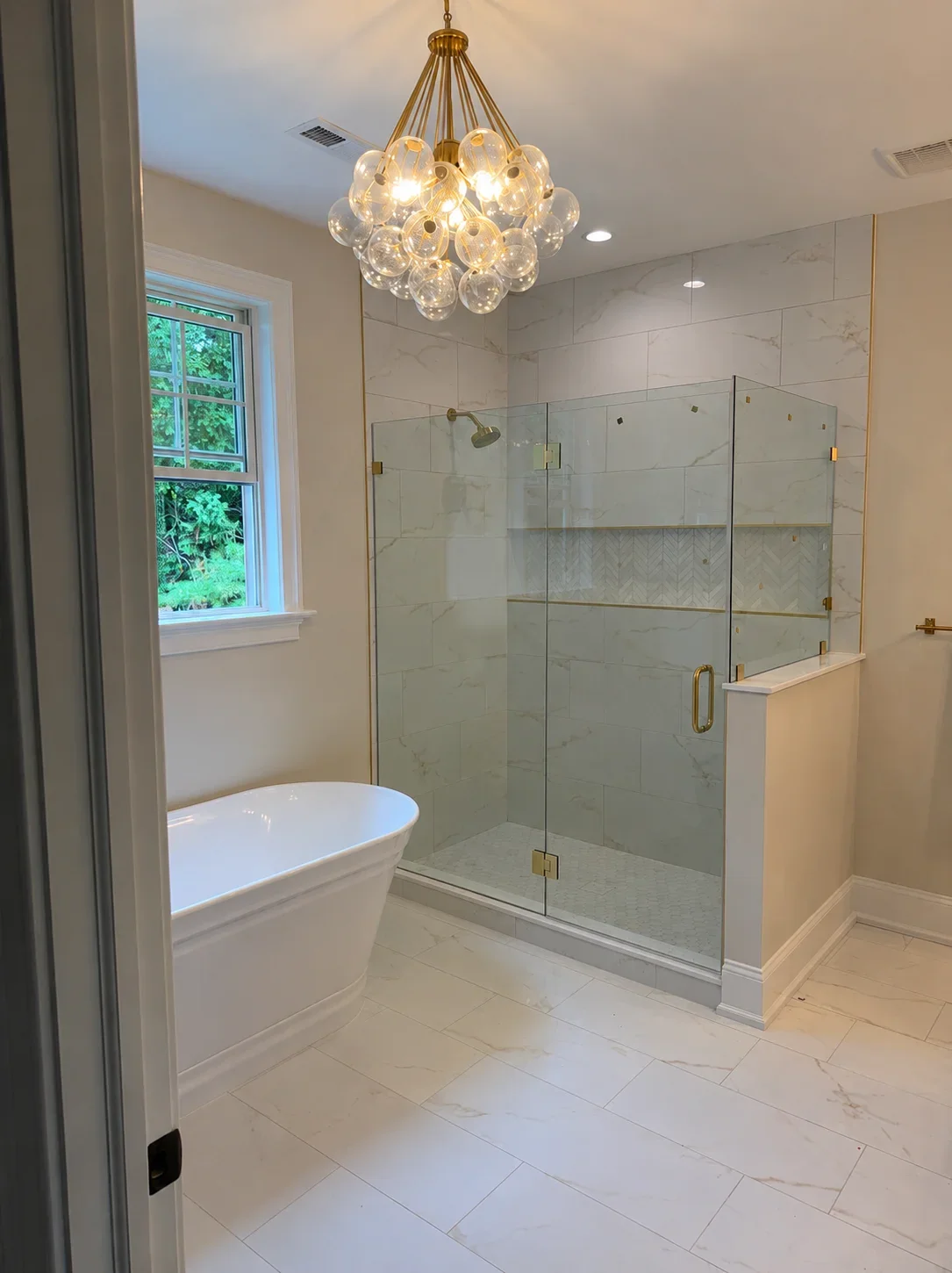 Marble bathroom with frameless glass shower, freestanding tub, and brass pendant light fixture
